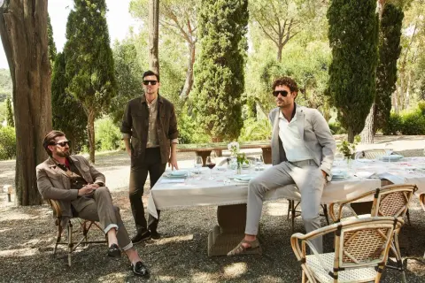 Tre uomini eleganti in un giardino. Il significato dei pantaloni chino è evidente nel loro stile casual-chic, perfetto per un pranzo all'aperto.