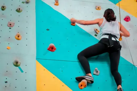 Une femme en tenue de sport fait de l'escalade sur un mur coloré, cherchant la prochaine prise.