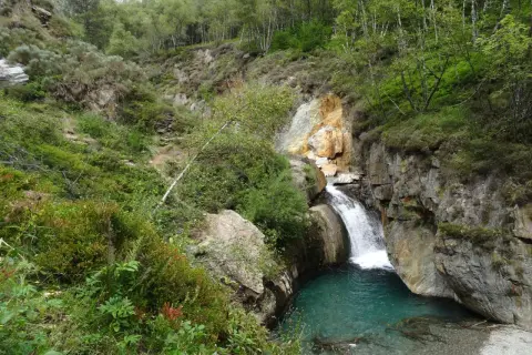 La cascade de l'Artigue dévale dans un bassin d'eau turquoise, entourée de roches et d'une végétation luxuriante.