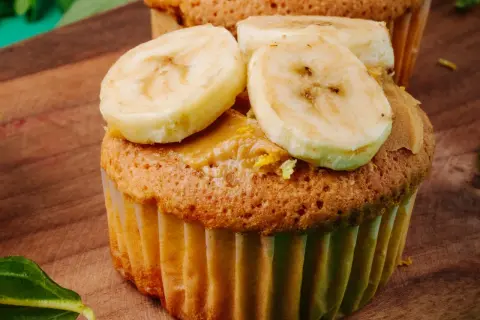 Pyszne muffinki bananowe fit z masłem orzechowym i plasterkami banana na drewnianej desce.