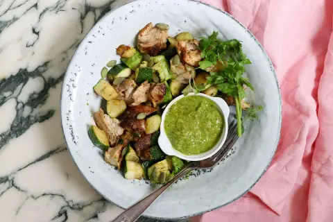 En tallrik med kyckling, zucchini och pumpafrön, serverad med en grön sås. En perfekt snabb nyttig lunch för en solig dag.