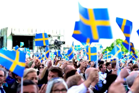 Stor folkmassa viftar med svenska flaggor. Många är lediga på nationaldagen och firar tillsammans.