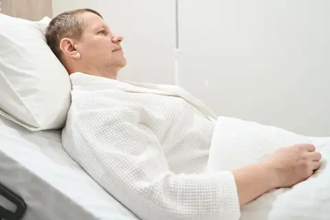 Mężczyzna w białym szlafroku leży w łóżku szpitalnym, przechodząc rekonwalescencję po usunięciu pęcherza moczowego.