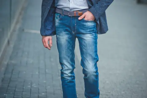 Mężczyzna w niebieskiej marynarce i modnych, przetartych jeansach. Różne rodzaje jeansów męskich można nosić na wiele sposobów.