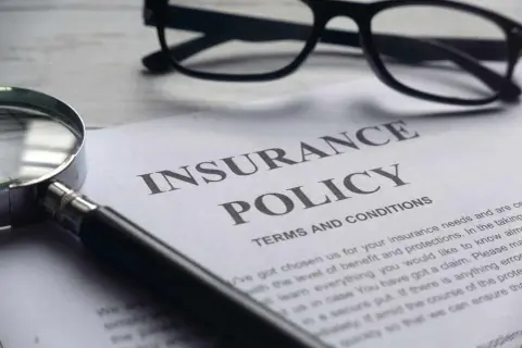 Okulary, lupa i dokument "Insurance Policy" symbolizują analizę polisy PZU po śmierci teścia.