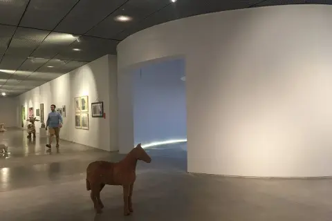 Un hombre pasea por una sala de exposiciones, admirando las obras de arte y una escultura de caballo. Una visita a los museos de Lugo.