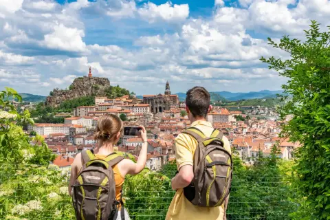Couple avec sacs à dos admire la vue panoramique du Puy-en-Velay, capturant le moment pour immortaliser leur visite à pied.