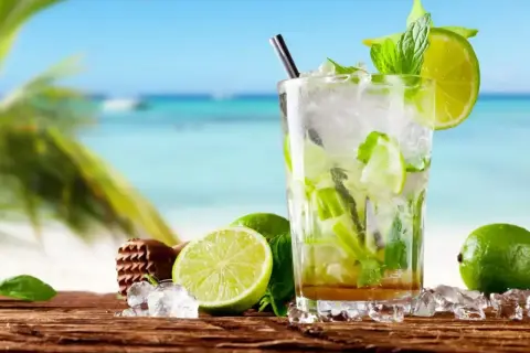 Szklanka orzeźwiającego mojito z limonką i miętą na tle plaży.