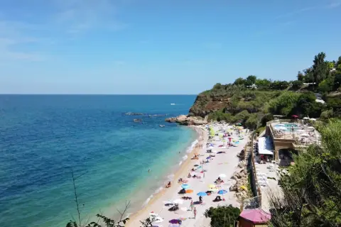 Spiaggia affollata con ombrelloni colorati, mare azzurro e scogliere verdi in Abruzzo. Un resort con piscina domina la scena.