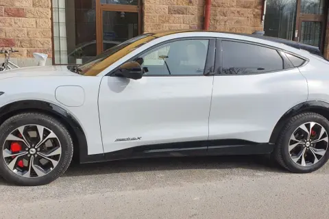 Vit Ford Mustang Mach-E står parkerad utanför en tegelbyggnad. En cykel syns i bakgrunden. Detta är en ford mustang mach-e test.