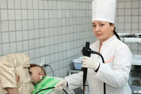 Lekarka w białym kitlu przygotowuje pacjenta do gastroskopii, trzymając endoskop.
