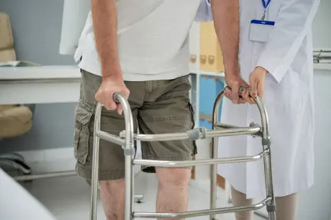 Un uomo anziano, con una sensazione di camminare storto, si appoggia a un deambulatore mentre un medico lo assiste.