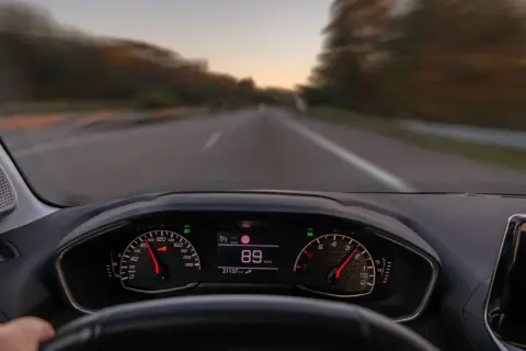 Widok z perspektywy kierowcy. Na desce rozdzielczej widać prędkościomierz wskazujący 89 km/h. To właśnie co robimy podczas jazdy samochodem.