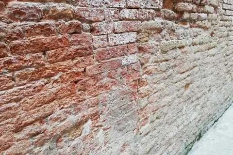 Un muro che sfarina rimedi, con mattoni rossi e bianchi consumati dal tempo, che raccontano storie antiche.
