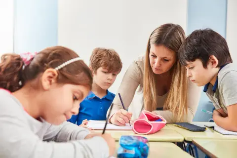 Lehrerin hilft Kindern in der Schule beim Schreiben.