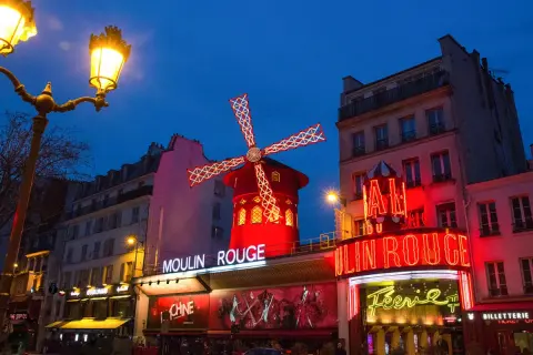 Le Moulin Rouge illuminé la nuit. La durée du spectacle est une question que beaucoup se posent avant de venir admirer ce lieu emblématique.