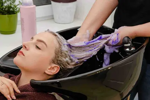 Kobieta w salonie fryzjerskim, jej włosy są myte fioletowym szamponem.