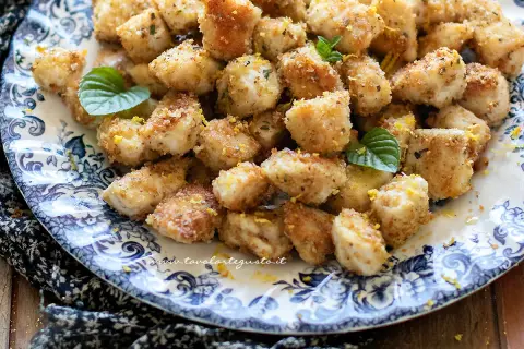 Bocconcini di pollo dorati e croccanti, guarniti con scorza di limone e foglie di menta fresca su un piatto decorato.
