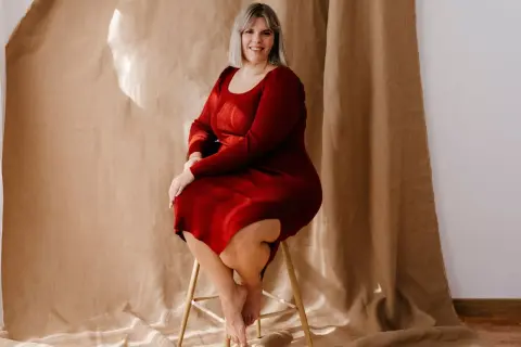 Uśmiechnięta kobieta w czerwonej sukience dresowej plus size siedzi na stołku.
