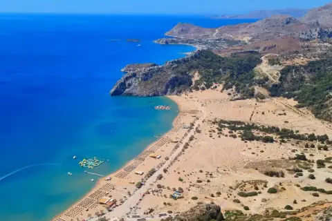 Widok na zatokę z turkusową wodą, piaszczystą plażą pełną leżaków i parasoli, wodnym placem zabaw. Jedna z najlepszych plaż w Grecji.