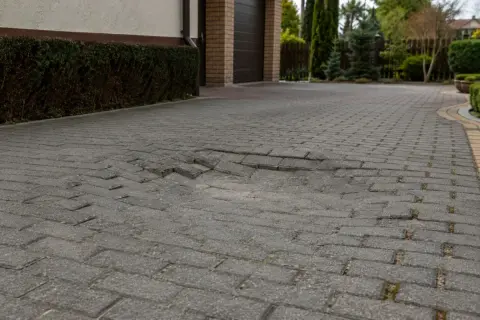 Zapadnięta kostka brukowa na podjeździe, z widocznym zagłębieniem i nierównościami.