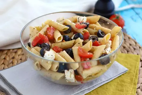En härlig italiensk pastasallad med penne, tomater, svarta oliver och fetaost i en glasskål. Perfekt för en lätt lunch.