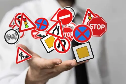 Main de personne tenant une multitude de panneaux de signalisation routière, dont certains indiquent la signification panneau interdiction poids lourds.