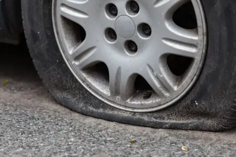 Pneu à plat sur la route, signe d'une perte de pression. La jante en alliage est visible, le pneu est complètement dégonflé.