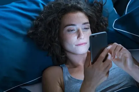 Dziewczyna leży w łóżku, przeglądając telefon. Może szuka wierszy na dobranoc dla dziewczyny, by wysłać je ukochanej.