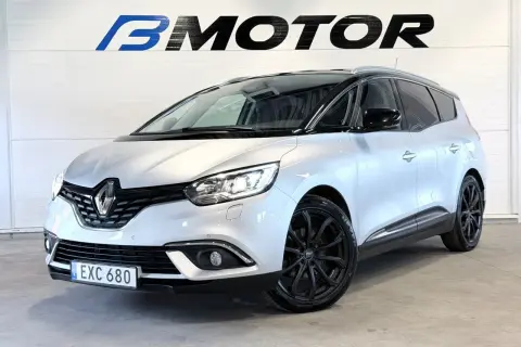 En silverfärgad Renault Grand Scénic med svarta fälgar står framför en vägg med logotypen B MOTOR.