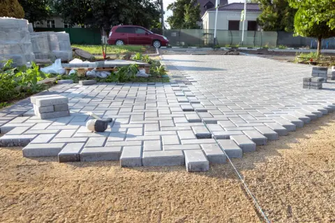 Układanie kostki brukowej na podwórku, widoczny młotek i stosy kostki.