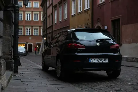 Czarny Alfa Romeo 147 na wąskiej uliczce. Czyj to numer rejestracyjny samochodu? SY 6904K.