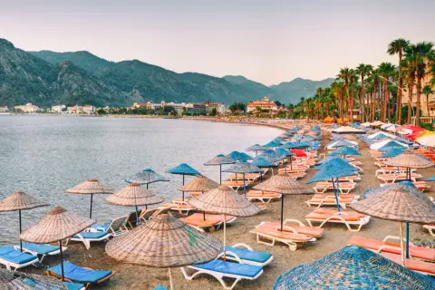 Plaża w Marmaris z rzędami leżaków i parasoli, idealne miejsce na relaks. W tle góry i hotele.