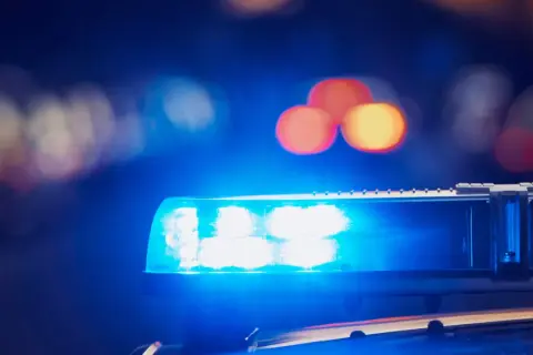 Niebieskie światła policyjne migają, symbolizując co to jest dozór policyjny. Rozmyte światła miasta w tle.
