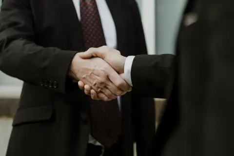 Dwaj mężczyźni w garniturach ściskają sobie dłonie. To symbol porozumienia, jak w art. 180 kpk.