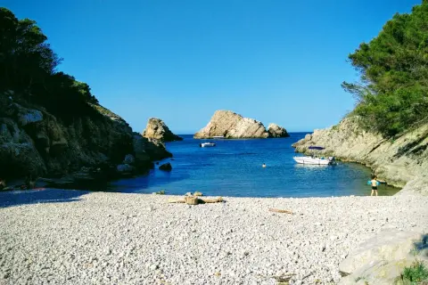 La cala Ferriol, con su playa de guijarros y aguas cristalinas, invita a disfrutar del sol y el mar. Barcas y bañistas comparten este paraíso.