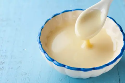 Cuchara con leche evaporada, un ingrediente cremoso y dulce, ideal para postres.
