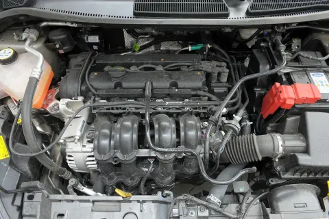 Silnik Ford Fiesta 2015. Widok komory silnika z widocznym kolektorem dolotowym, alternatorem i akumulatorem.
