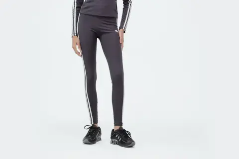 Leggings Adidas 3 stripes grigi, con logo e strisce bianche, abbinati a sneakers nere.