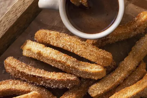 Churros caseros espolvoreados con azúcar junto a una taza de chocolate caliente.