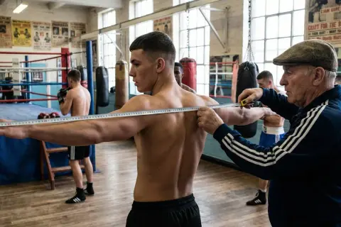 A coach measures a boxer's reach in a gym, a crucial step in how reach is measured in boxing.