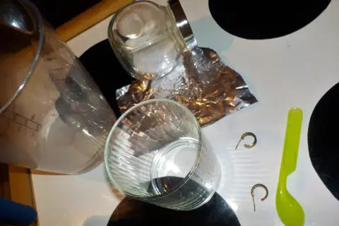 Szklanka, folia aluminiowa, sól, łyżeczka i kolczyki na blacie.