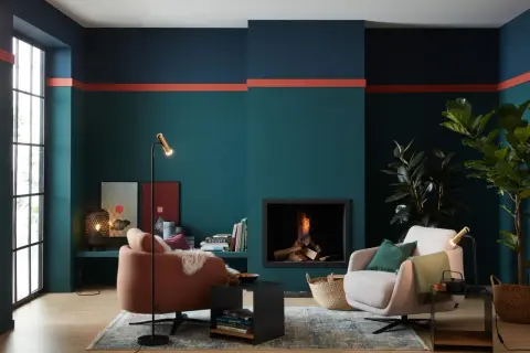Moderne Wohnzimmer-farbgestaltung wand mit petrol, dunkelblau und korallenroten Akzenten. Gemütliche Sessel und Kamin sorgen für Wohlfühlatmosphäre.