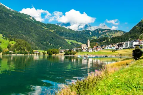 Incantevole lago alpino con barche a vela, circondato da verdi montagne e pittoreschi borghi Trentino Alto Adige.
