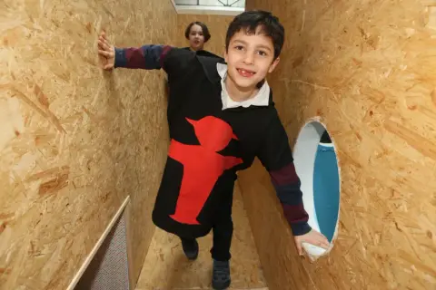 Chłopiec w bluzie z czerwonym motywem przemierza drewniany labirynt, jedną z wielu atrakcji dla dzieci w Berlinie.