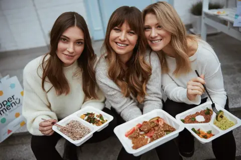 Trzy uśmiechnięte kobiety z pudełkami zdrowych posiłków. To idealna dieta na schudnięcie, która ułatwia osiągnięcie wymarzonej sylwetki.
