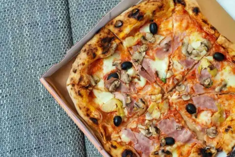 Pyszna pizza capricciosa z szynką, pieczarkami, karczochami i oliwkami w pudełku.