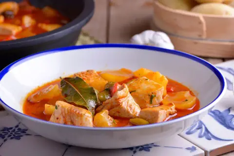 Un plato humeante de patatas con bonito, con trozos de pescado tierno y patatas en una salsa roja sabrosa, adornado con hojas de laurel.