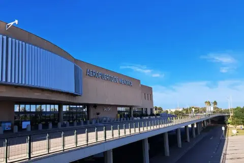 Nowoczesny budynek lotniska Aeropuerto de Menorca z napisem "AEROPUERTO DE MENORCA" i podjazdem pod niebo.
