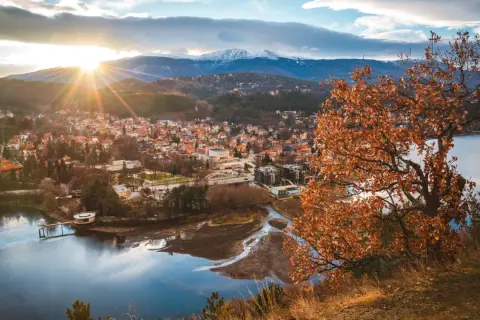 Widok na miasteczko nad jeziorem, góry w tle. Idealne miejsce, gdzie na wakacje w sierpniu, choć liście drzew już brązowe.